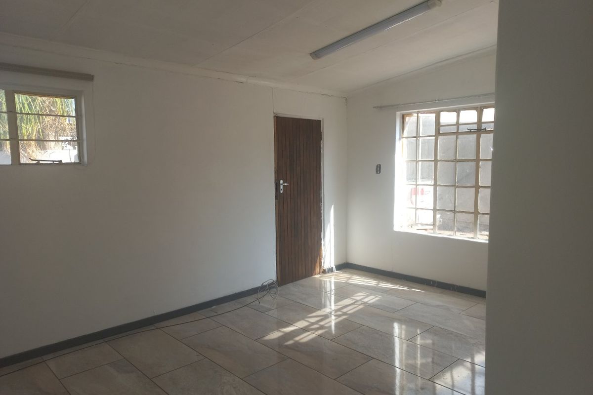 An empty, sunlit living area featuring tiled flooring, a timber door, and grid-pattern windows, offering a blank canvas for interior design.