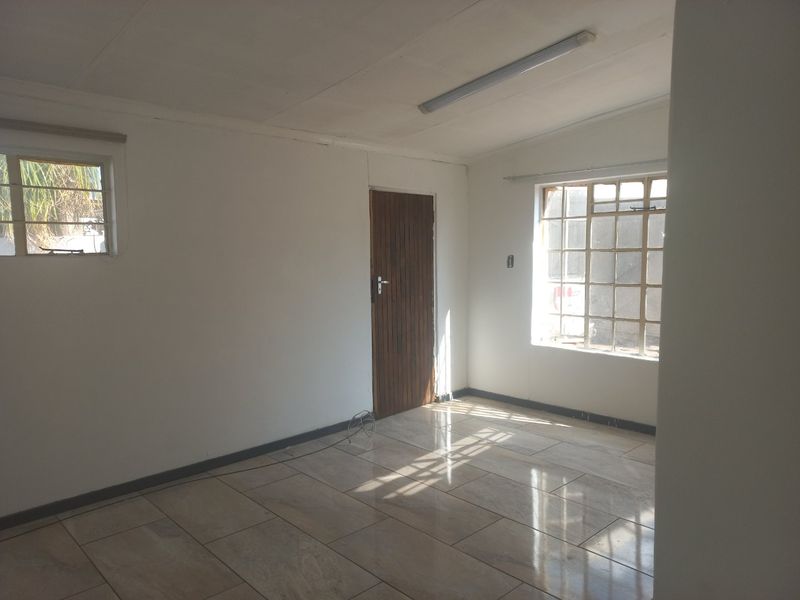 An empty, sunlit living area featuring tiled flooring, a timber door, and grid-pattern windows, offering a blank canvas for interior design.