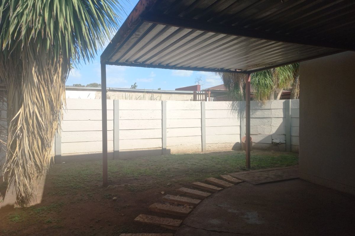 Rear outdoor area featuring a covered patio with a corrugated metal roof, concrete slab, and a precast concrete boundary wall.