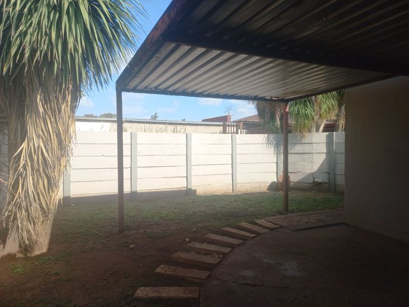 Rear outdoor area featuring a covered patio with a corrugated metal roof, concrete slab, and a precast concrete boundary wall.
