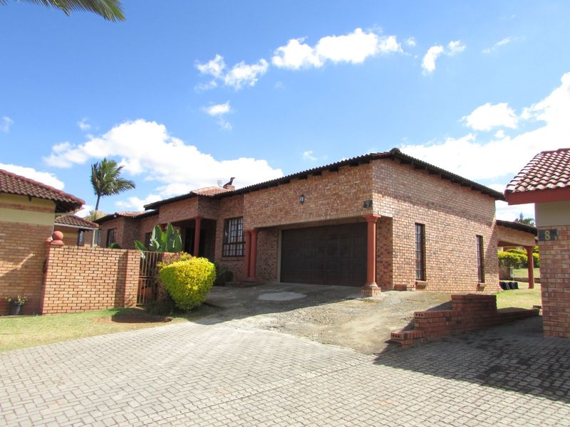 Front view of a face brick house featuring a double garage, paved driveway, and a covered entrance area within a residential complex.