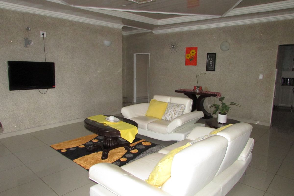 A spacious living room featuring tiled flooring, a recessed ceiling design, and wall-mounted lighting fixtures.