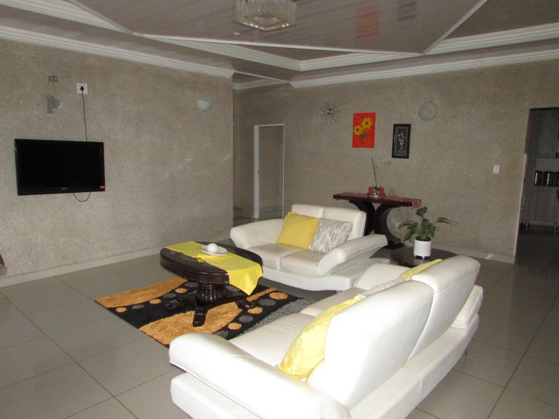 A spacious living room featuring tiled flooring, a recessed ceiling design, and wall-mounted lighting fixtures.