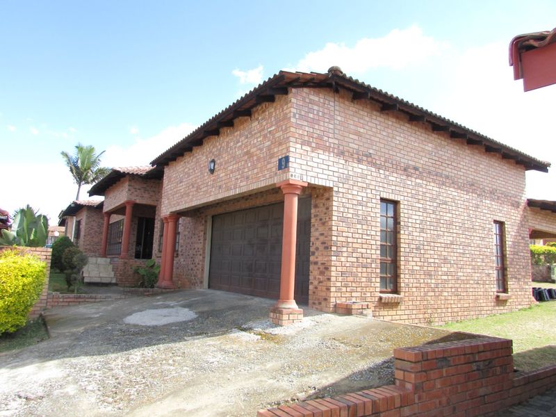Front exterior view of a face brick house featuring a double garage, concrete driveway, and decorative columns under a tiled roof.