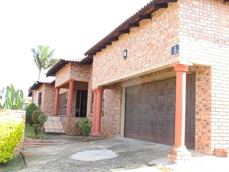 Front elevation of a face brick house featuring a garage, concrete driveway, and decorative columns under a tiled roof.