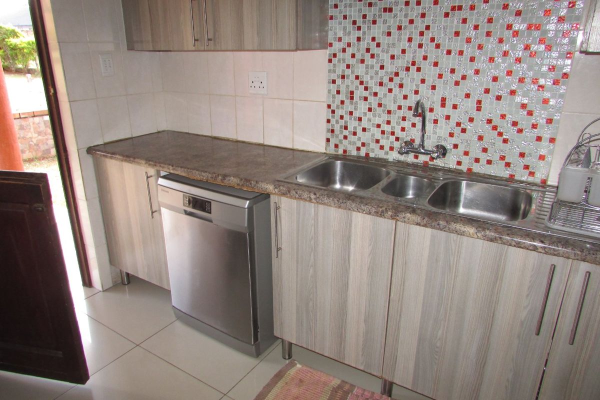 Kitchen area featuring wood-look laminate cabinetry, a double stainless steel sink, mosaic tile backsplash, and tiled flooring with direct access to the exterior.
