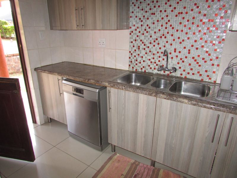 Kitchen area featuring wood-look laminate cabinetry, a double stainless steel sink, mosaic tile backsplash, and tiled flooring with direct access to the exterior.
