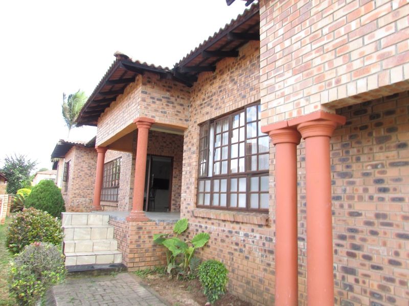 A classic face brick house exterior featuring a covered patio, decorative columns, and grid-pattern windows with a paved entrance walkway.
