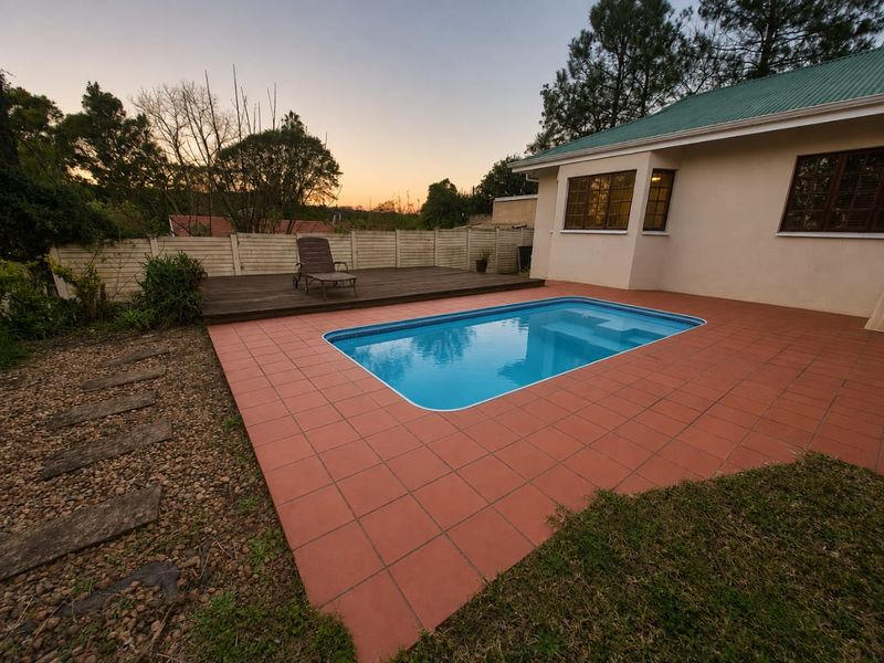 Outdoor pool area featuring a swimming pool, tiled surround, and raised timber deck, set against a private boundary wall and landscaped garden.