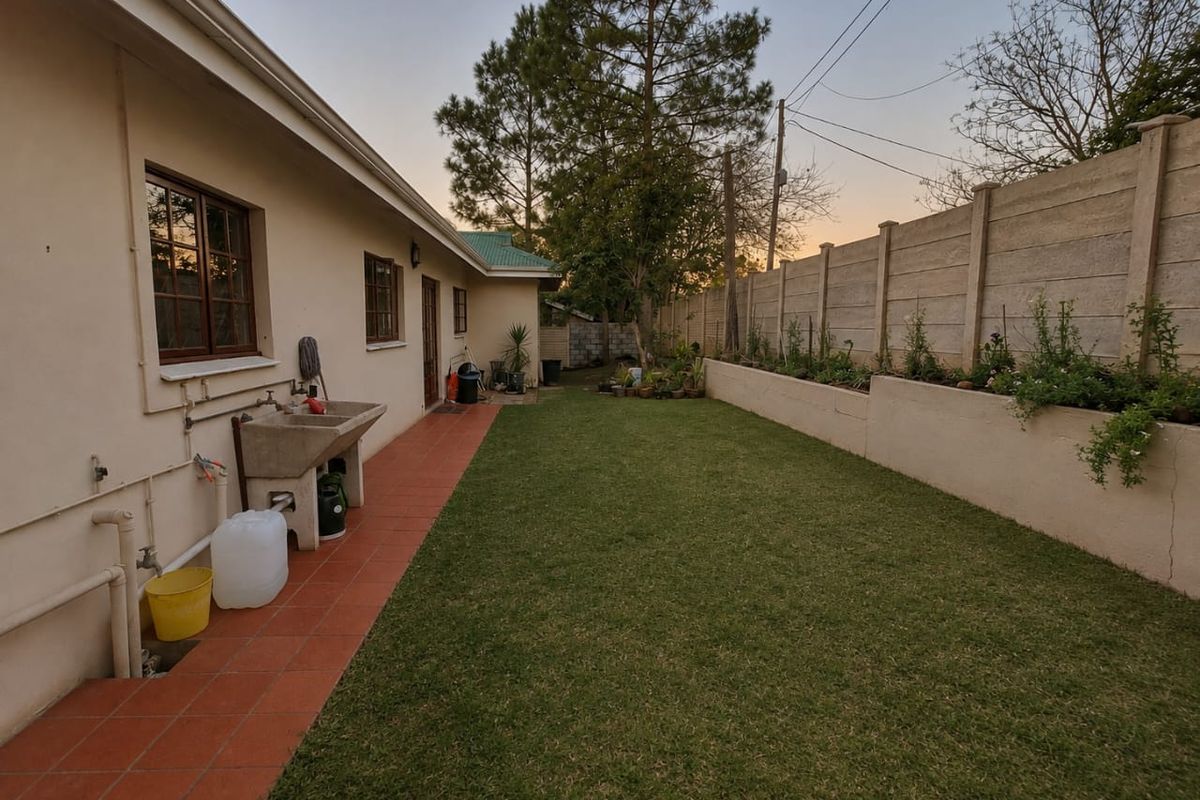 Rear garden area featuring a tiled patio, concrete utility sink, lawn, and a precast concrete boundary wall with a retaining planter.