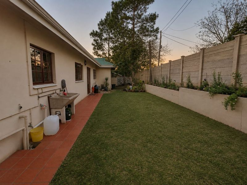 Rear garden area featuring a tiled patio, concrete utility sink, lawn, and a precast concrete boundary wall with a retaining planter.