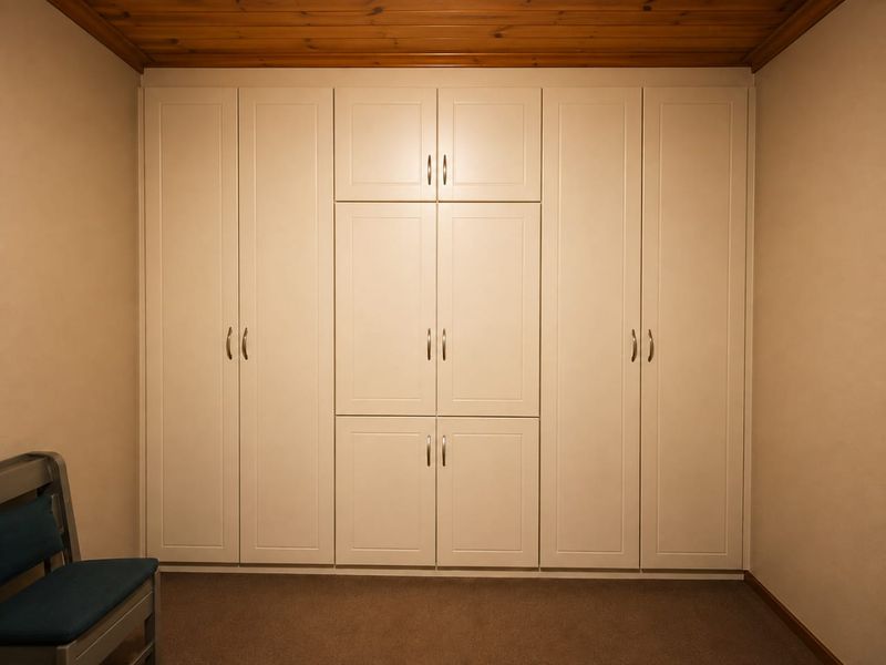 A bedroom featuring extensive floor-to-ceiling built-in cabinetry with a classic finish and a warm timber-paneled ceiling.