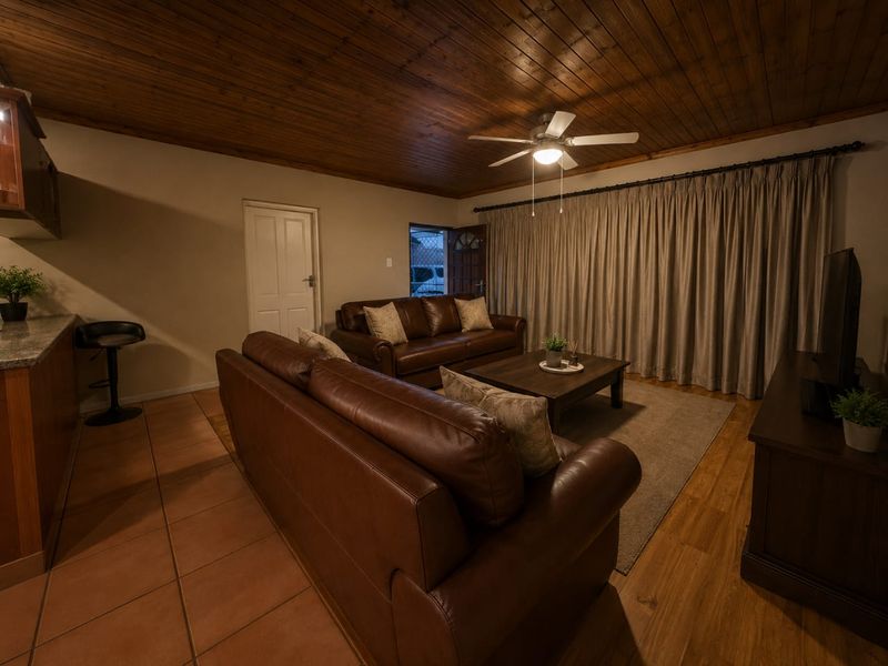 Open plan living area featuring a timber ceiling, ceiling fan, and a combination of tiled and laminate flooring with an integrated kitchen counter.