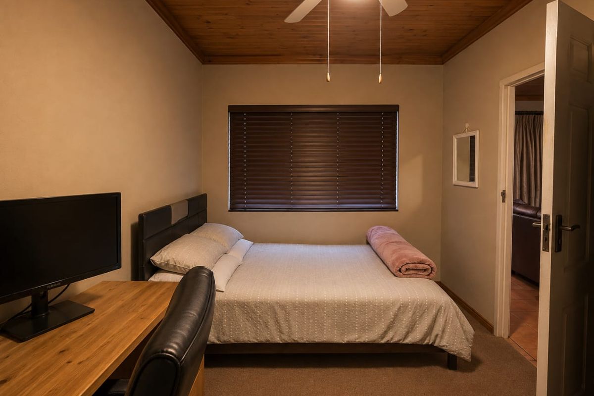 A cozy bedroom featuring a timber ceiling, ceiling fan, and venetian blinds, providing a warm and functional sleeping space.
