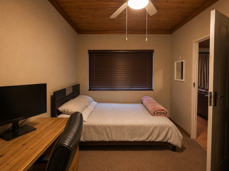 A cozy bedroom featuring a timber ceiling, ceiling fan, and venetian blinds, providing a warm and functional sleeping space.