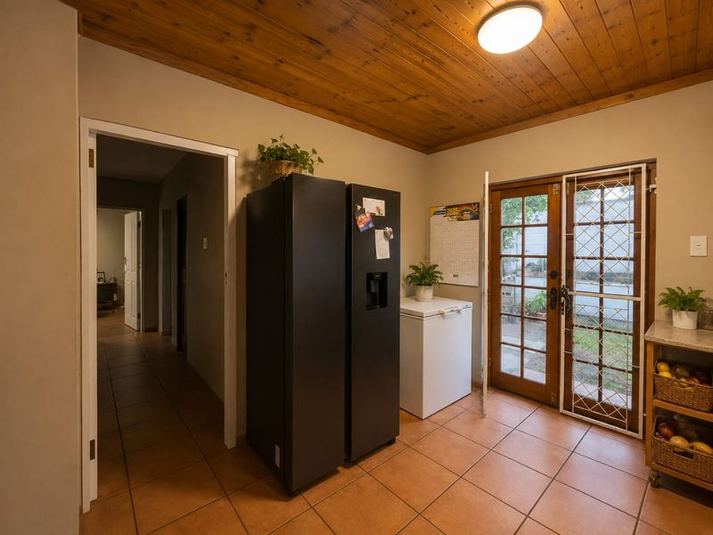 A functional scullery or utility area featuring tiled flooring, a timber-paneled ceiling, and direct access to the garden through timber-framed french doors.