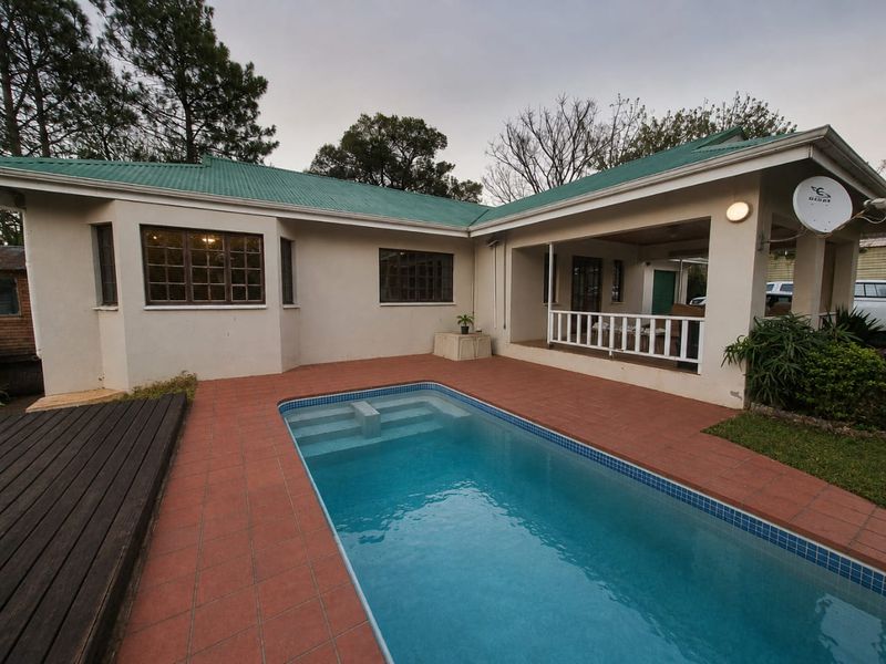 Rear exterior view featuring a swimming pool with tiled surround, a wooden deck, and a covered patio area under a metal roof.