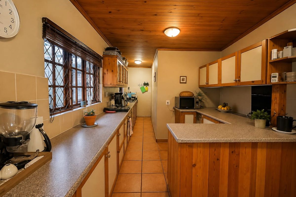 A functional kitchen featuring timber cabinetry, laminate countertops, tiled flooring, and a distinctive timber-paneled ceiling with leaded glass windows.