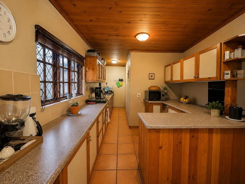 A functional kitchen featuring timber cabinetry, laminate countertops, tiled flooring, and a distinctive timber-paneled ceiling with leaded glass windows.