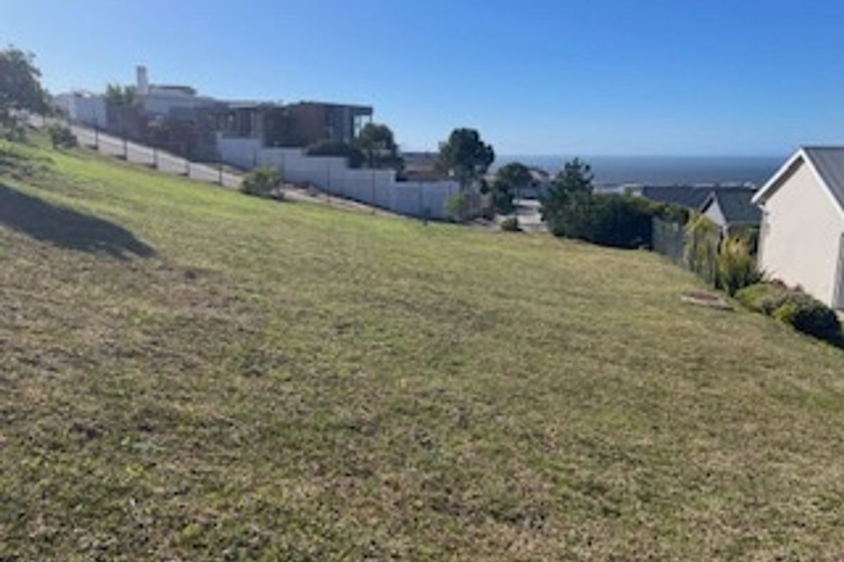 A sloped residential vacant land plot featuring perimeter fencing and distant ocean views, offering potential for tiered development.