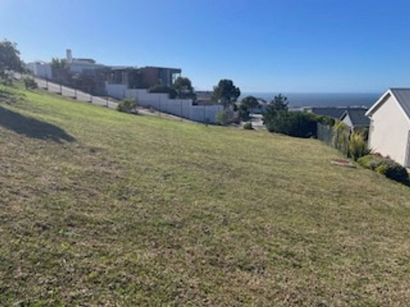 A sloped residential vacant land plot featuring perimeter fencing and distant ocean views, offering potential for tiered development.