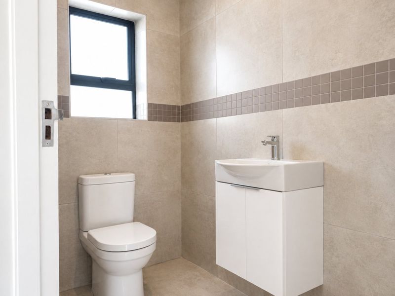 A modern, well-maintained bathroom featuring neutral wall tiles, a wall-mounted vanity with a basin, and a dual-flush toilet.