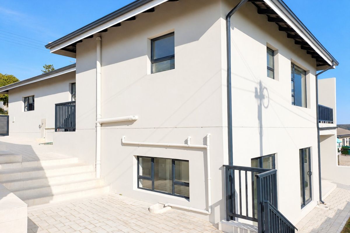 A well-maintained rear exterior view of the house featuring paved patio areas, modern aluminium window frames, and clean rendered wall finishes.
