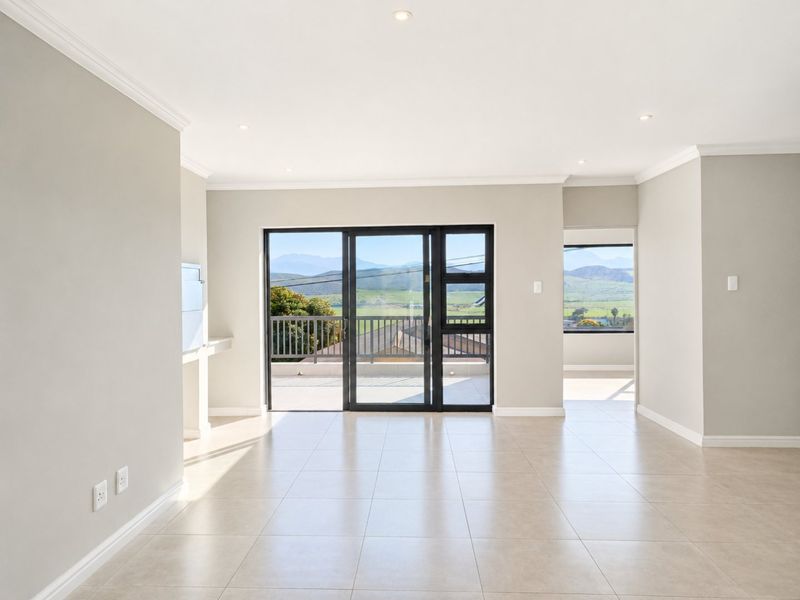 A bright, open-plan living area featuring neutral tiled floors, recessed lighting, and large sliding glass doors that open onto a balcony with scenic views.