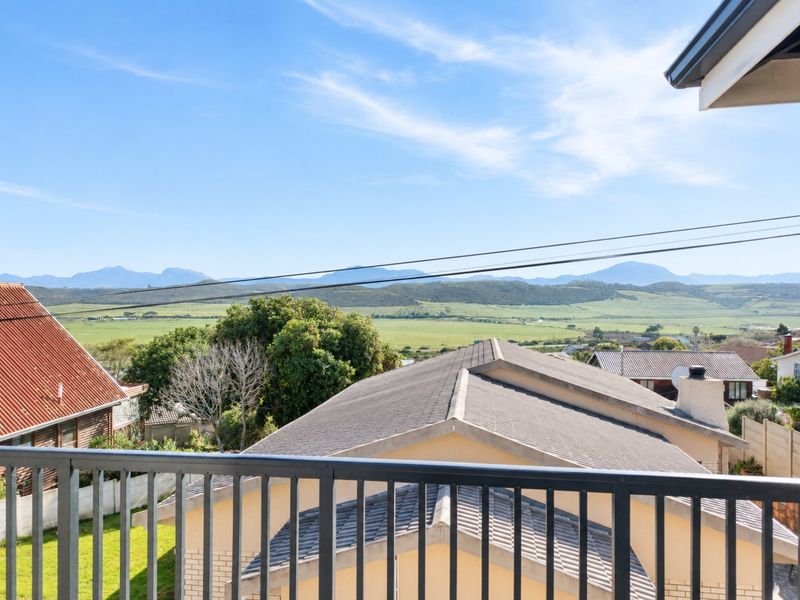 Elevated view from a balcony overlooking neighbouring rooftops and a scenic landscape with rolling hills in the distance.