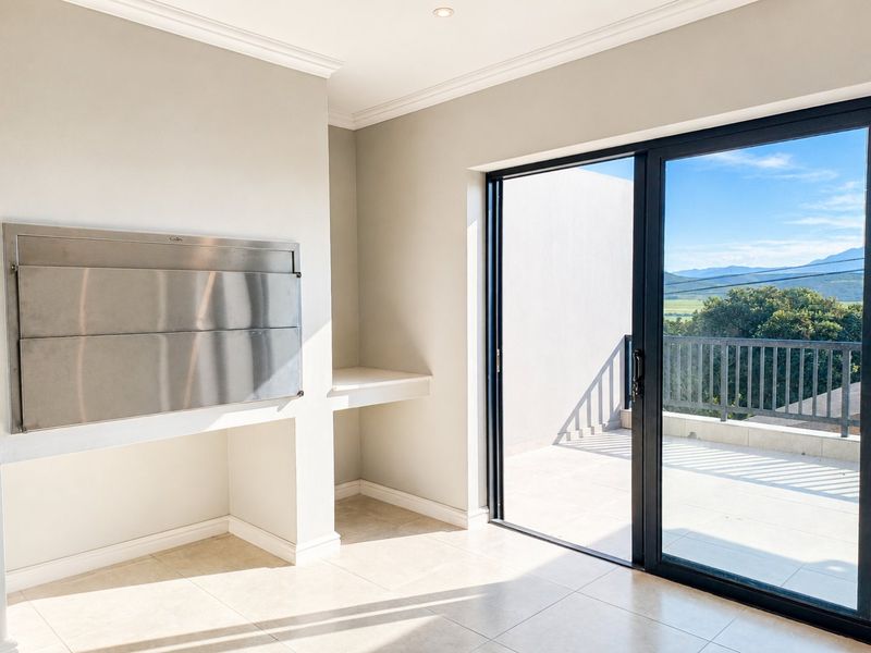 An indoor entertainment area featuring a built-in stainless steel braai, tiled flooring, and large sliding doors opening onto a balcony with scenic views.
