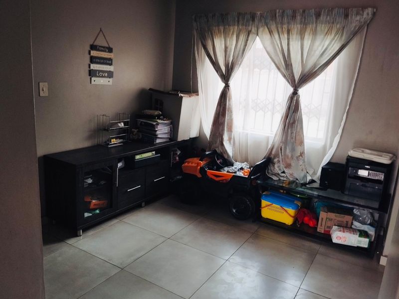 A living room area featuring neutral tiled flooring and a window fitted with security bars, providing natural light.