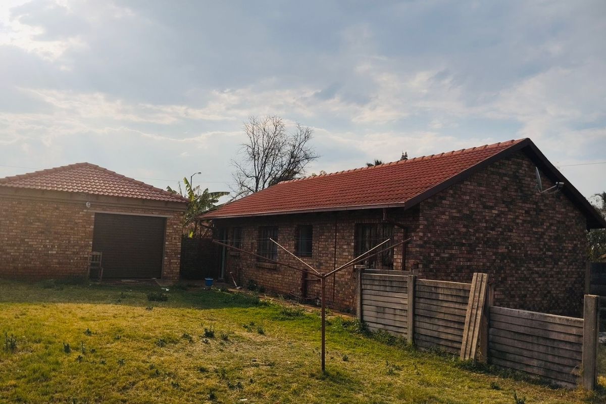Rear view of the property featuring a face brick exterior, tiled roof, detached garage, and surrounding garden area with perimeter walling.