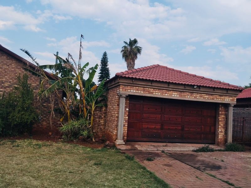 Front view of a brick house featuring a double garage with a tiled roof and a paved driveway.