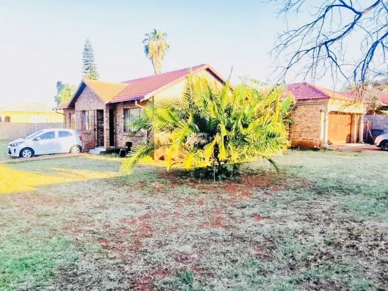 A single-story face-brick house featuring a tiled roof, attached garage, and security bars, set on a spacious residential plot with established garden.