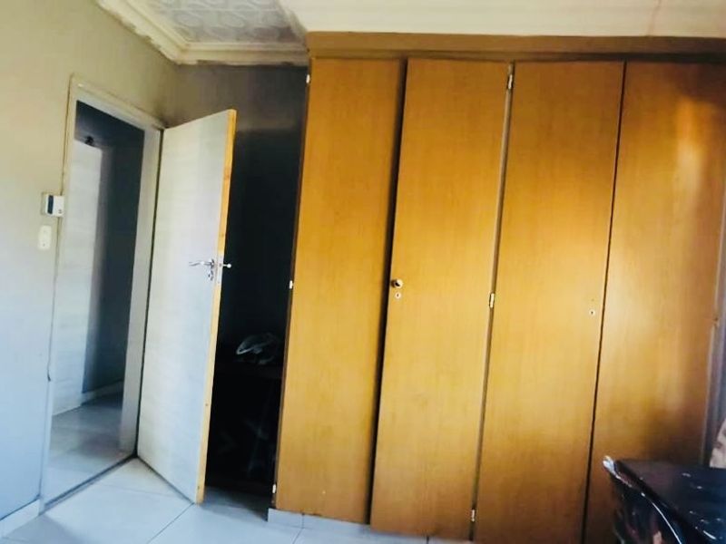 A bedroom featuring built-in wooden cupboards, tiled flooring, and decorative ceiling cornicing.