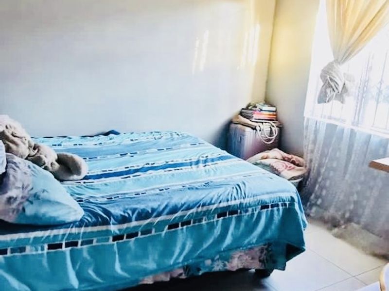 A bedroom featuring tiled flooring, textured ceiling tiles, and a window fitted with security bars.