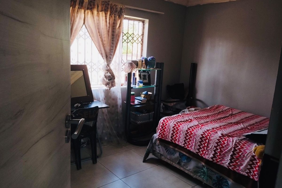 A compact bedroom featuring tiled flooring and security bars on the window, requiring minor cosmetic updates to the ceiling and wall finishes.