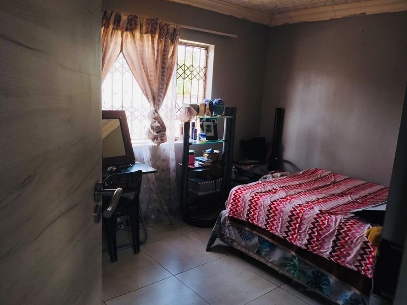 A compact bedroom featuring tiled flooring and security bars on the window, requiring minor cosmetic updates to the ceiling and wall finishes.