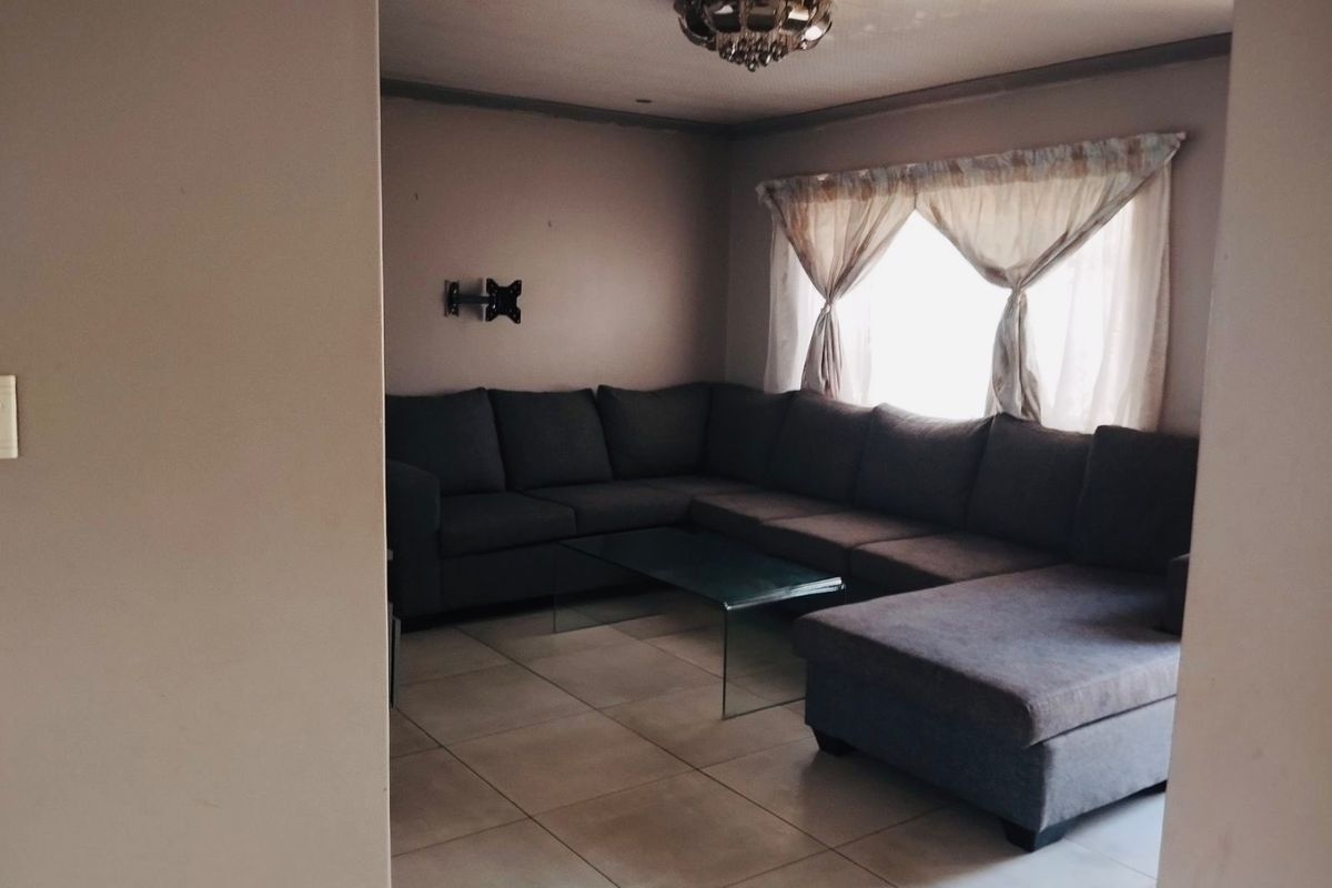 A living room featuring tiled flooring and a wall-mounted television bracket, viewed from an adjacent hallway.