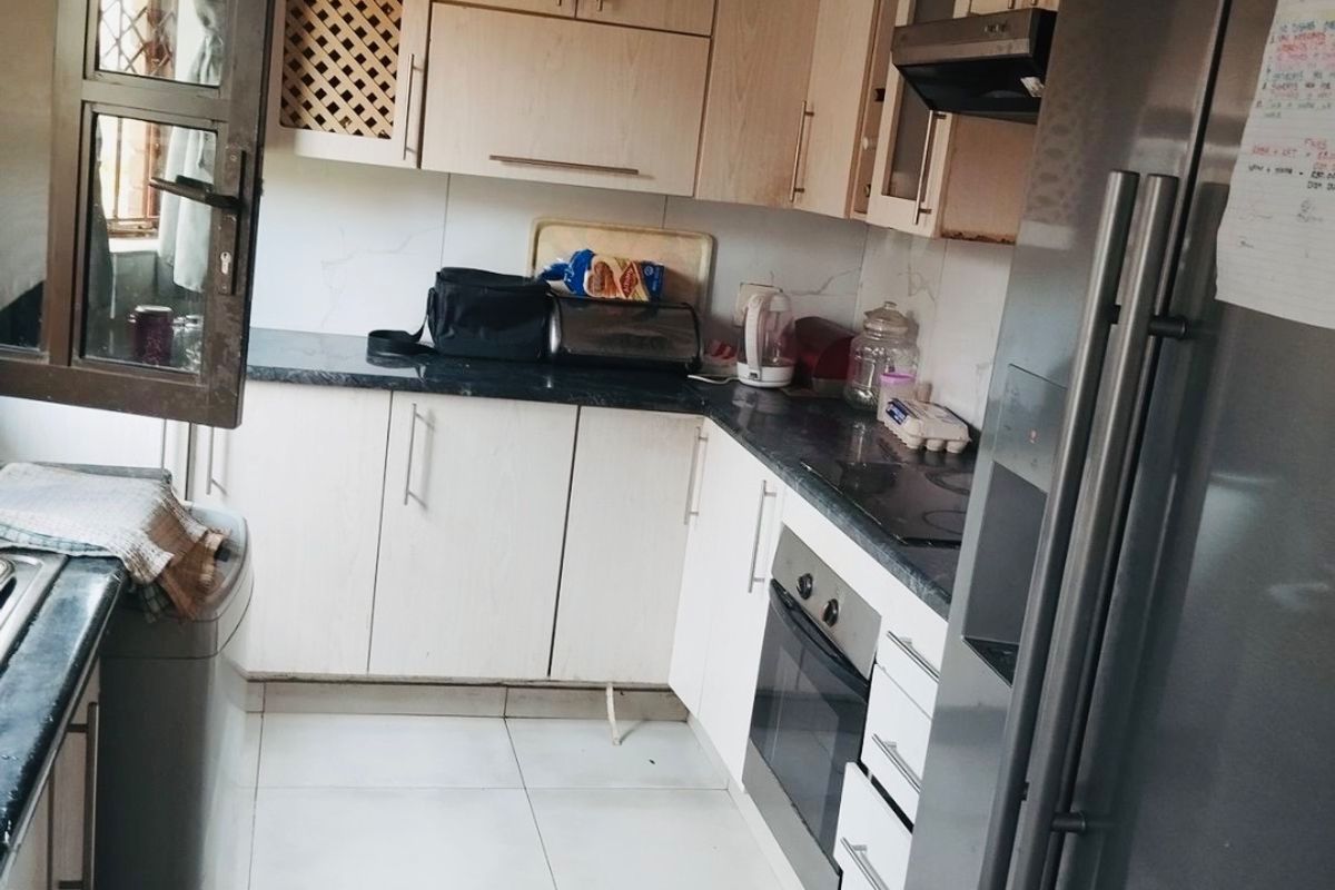 A functional kitchen featuring light wood-finish cabinetry, dark countertops, built-in oven, hob, and extractor fan with tiled flooring.