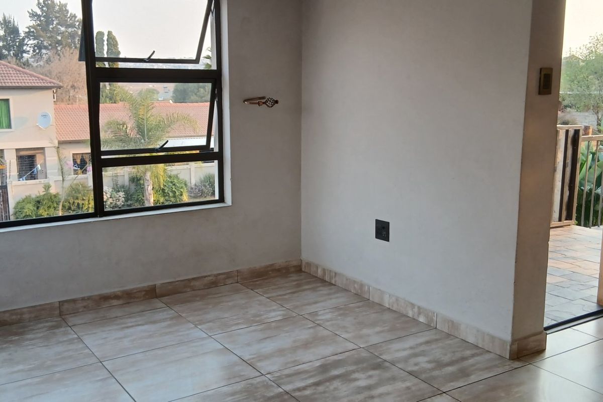 An empty bedroom featuring tiled flooring, large aluminium windows, and direct access to an outdoor balcony area.