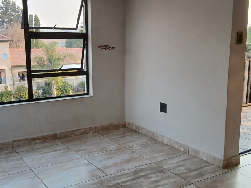 An empty bedroom featuring tiled flooring, large aluminium windows, and direct access to an outdoor balcony area.