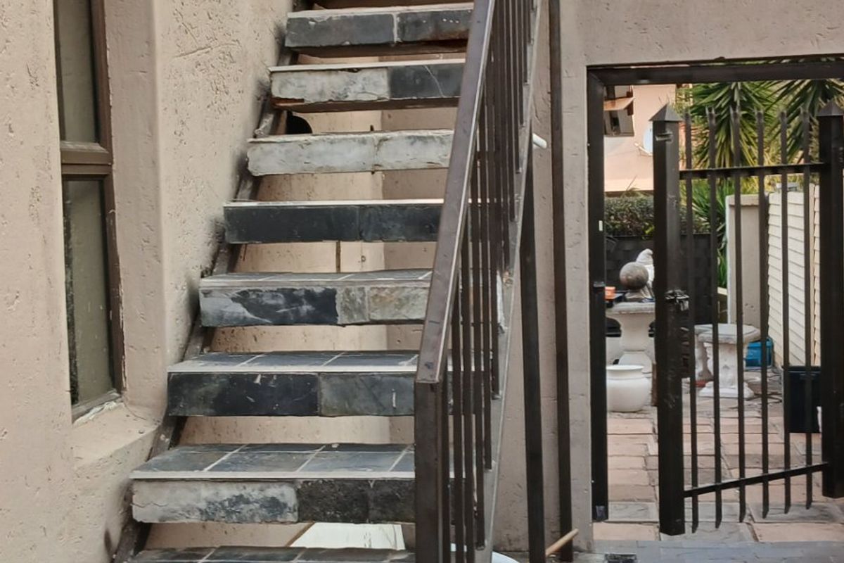 Exterior rear view featuring an external staircase with tiled steps, metal balustrade, and a paved courtyard area with a drainage channel.