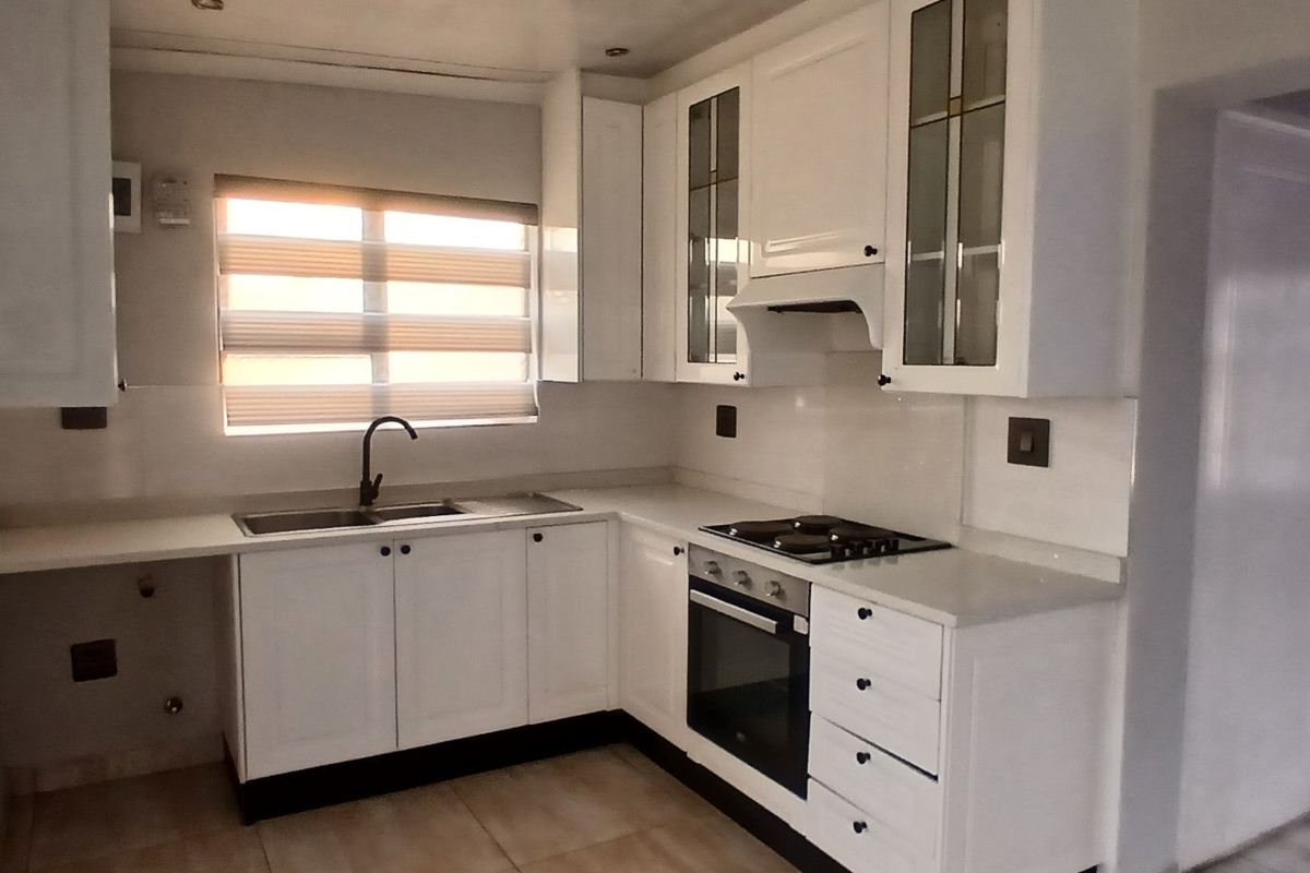 A clean, modern kitchen featuring white cabinetry, stone countertops, built-in oven, gas hob, and an undermount sink with a contemporary mixer tap.