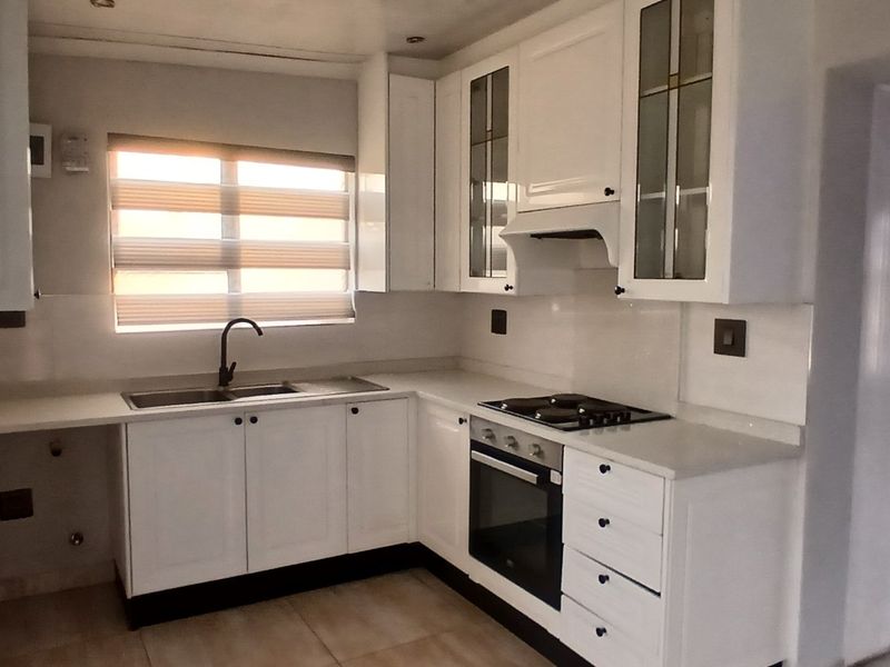 A clean, modern kitchen featuring white cabinetry, stone countertops, built-in oven, gas hob, and an undermount sink with a contemporary mixer tap.
