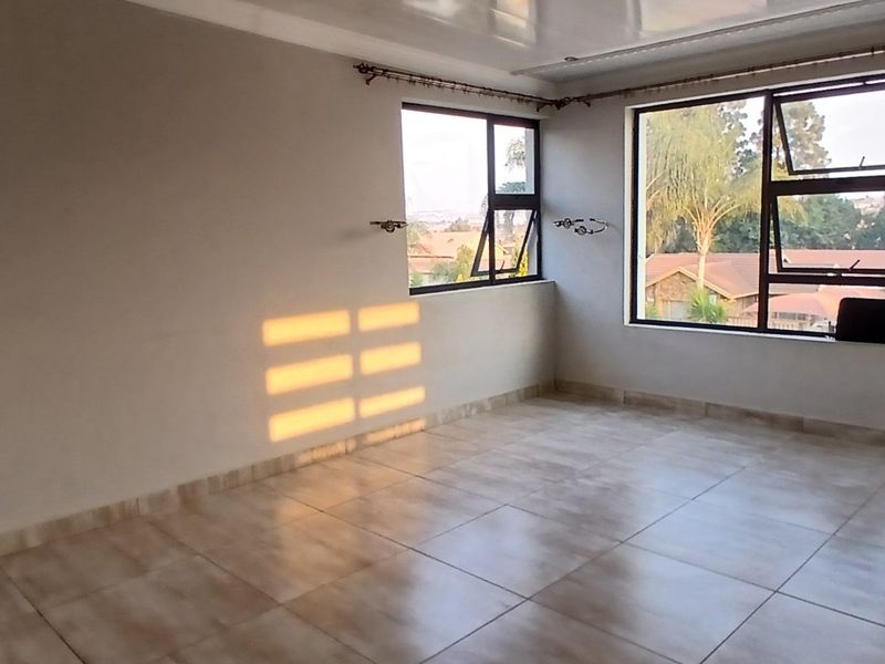 A bright, empty living area featuring neutral tiled flooring and large aluminium-framed windows that provide ample natural light.