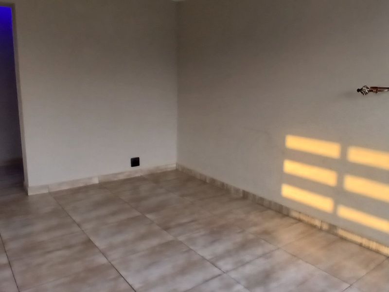 An empty bedroom featuring neutral tiled flooring, clean walls, and natural light entering through a side window.
