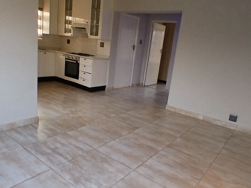 An open-plan living area featuring tiled flooring and a functional kitchen with built-in cabinetry, oven, and hob.