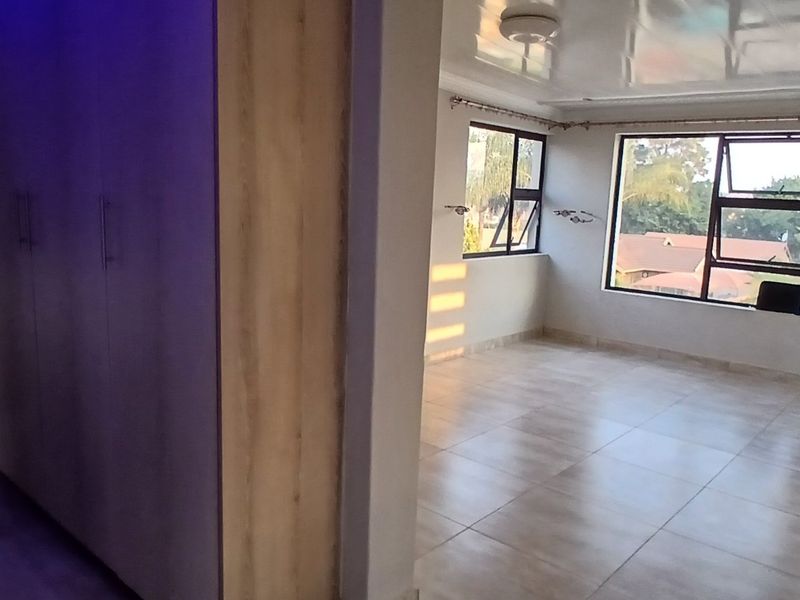 An empty, well-lit living area featuring tiled flooring, built-in cupboards, and large windows providing natural light.