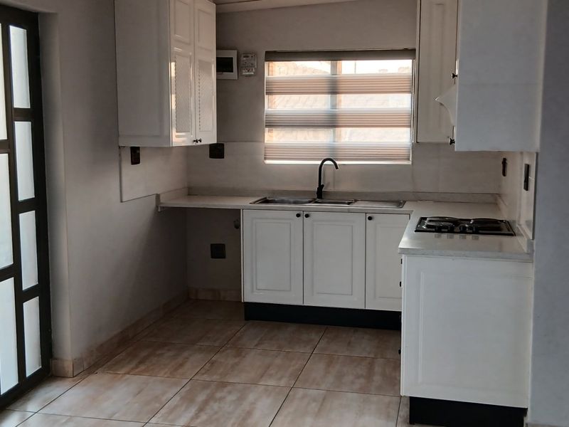 A clean, functional kitchen featuring white built-in cabinetry, a double sink with a modern mixer tap, a built-in hob, and tiled flooring.